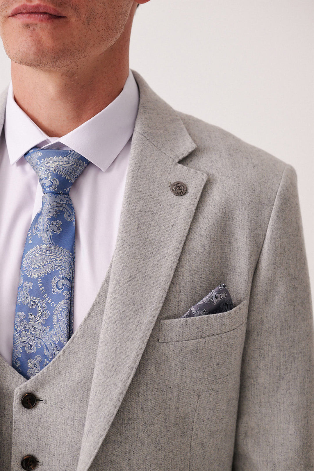 A man wearing the marcdarcy ARCHIE Silver Tweed Three Piece Suit, featuring a matching vest, white shirt, blue paisley tie, and pocket square. Only his lower face and torso are visible.