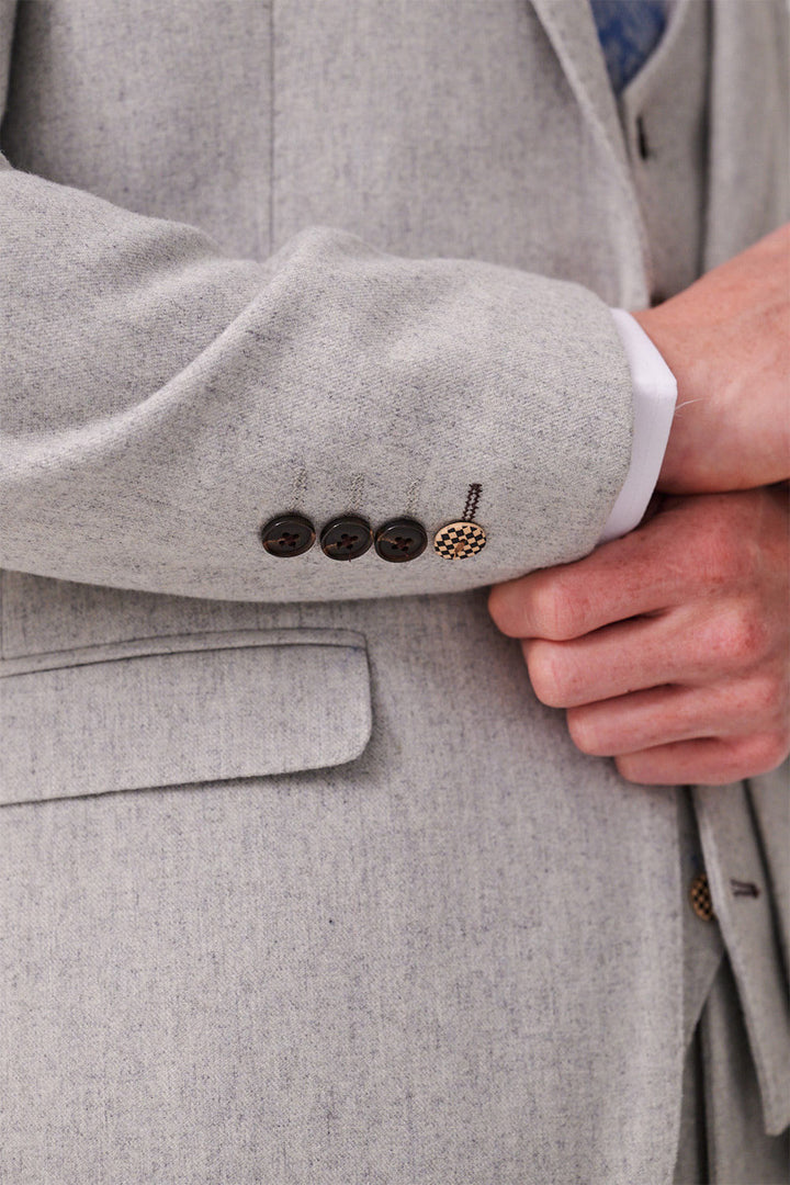 A close-up of a hand adjusting the cuff of marcdarcy's ARCHIE Silver Tweed Three Piece Suit, highlighting its slim fit, four dark sleeve buttons, and a visible white shirt cuff.
