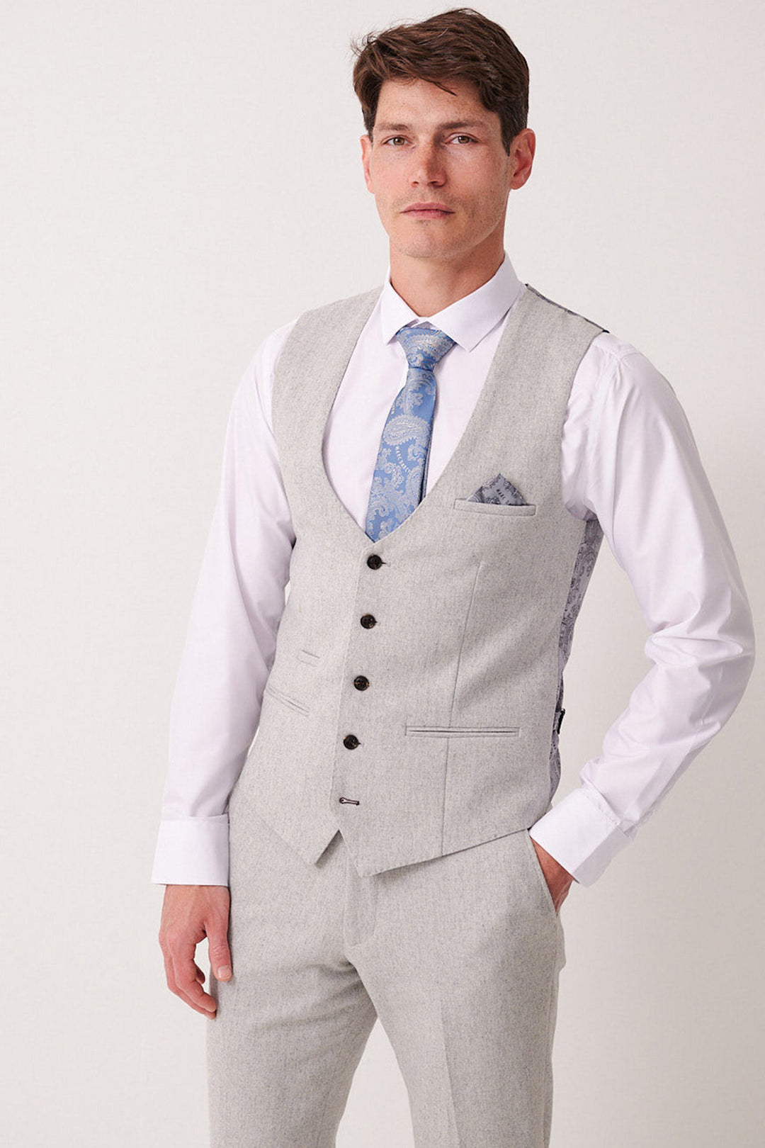 A man wears the Marc Darcy ARCHIE Silver Tweed Waistcoat with matching trousers, a white dress shirt, light blue patterned tie, and pocket square, standing against a plain light background.