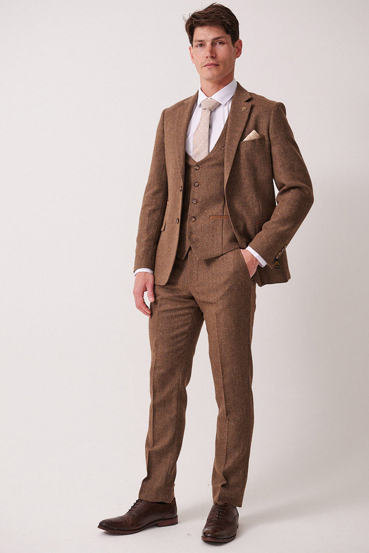 A man with short brown hair and a neutral expression wears the marcdarcy DEAN Tan Tweed Three Piece Suit—a slim fit suit with matching vest—paired with a white shirt, white tie, and dark brown shoes, against a plain background.