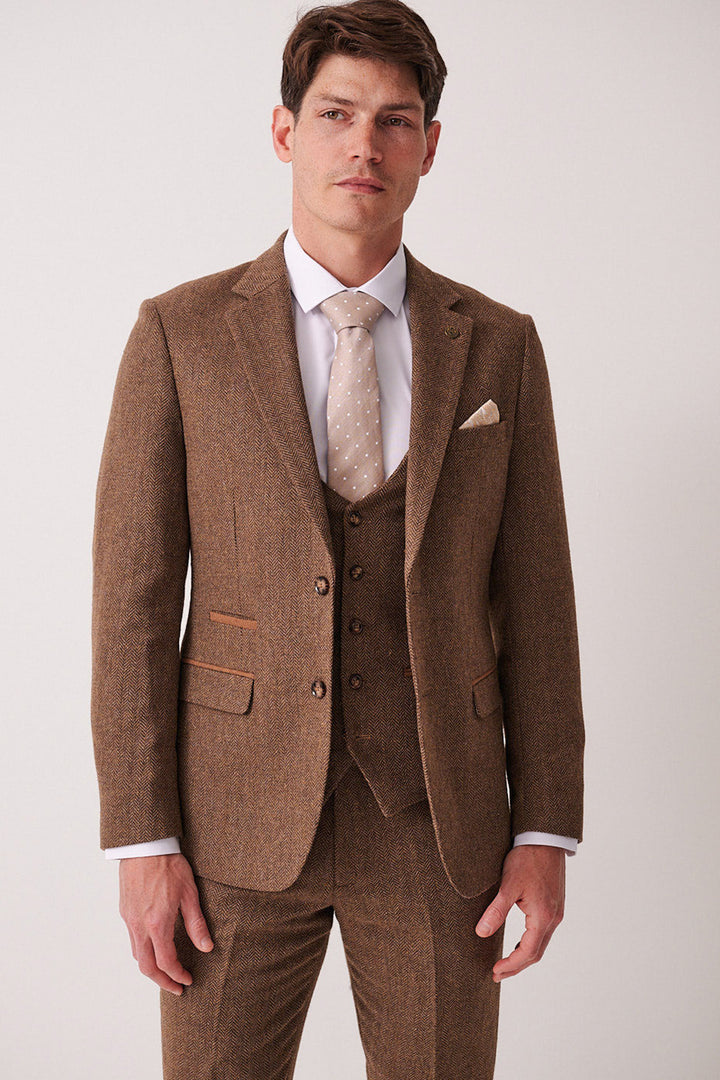 A man wears the marcdarcy DEAN Tan Tweed Blazer with a white dress shirt and beige polka dot tie, standing against a plain light background and looking at the camera with a neutral expression.
