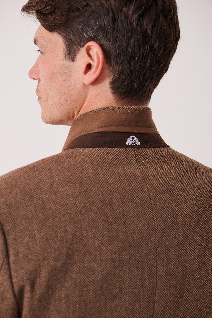 A man with short brown hair is seen from the back wearing the marcdarcy DEAN Tan Tweed Three Piece Suit, featuring a slim fit and a raised collar with a decorative emblem.