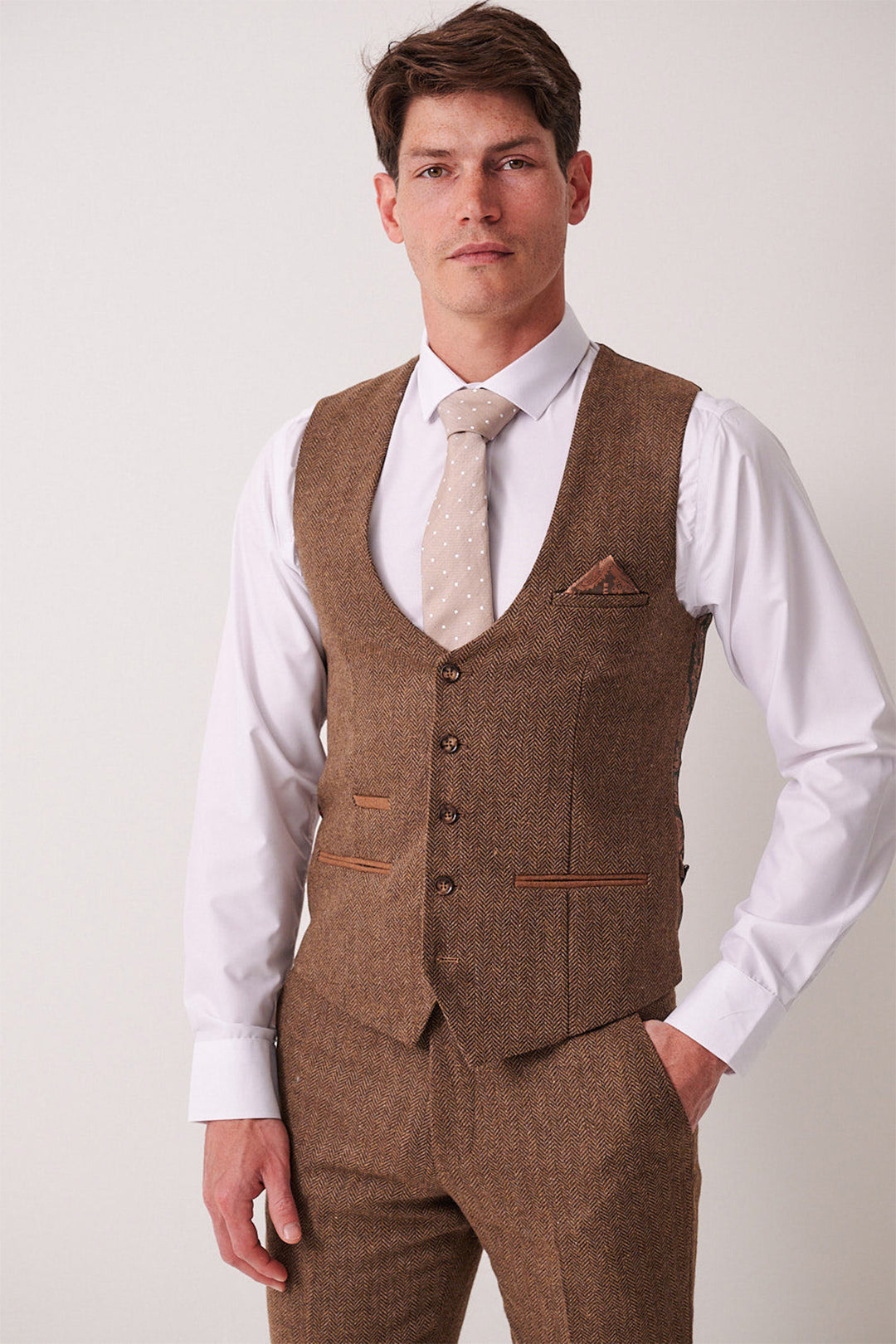 A man wears the marcdarcy DEAN Tan Tweed Three Piece Suit—featuring a slim fit vest and trousers, white dress shirt, and a light beige polka dot tie—standing against a plain light background.