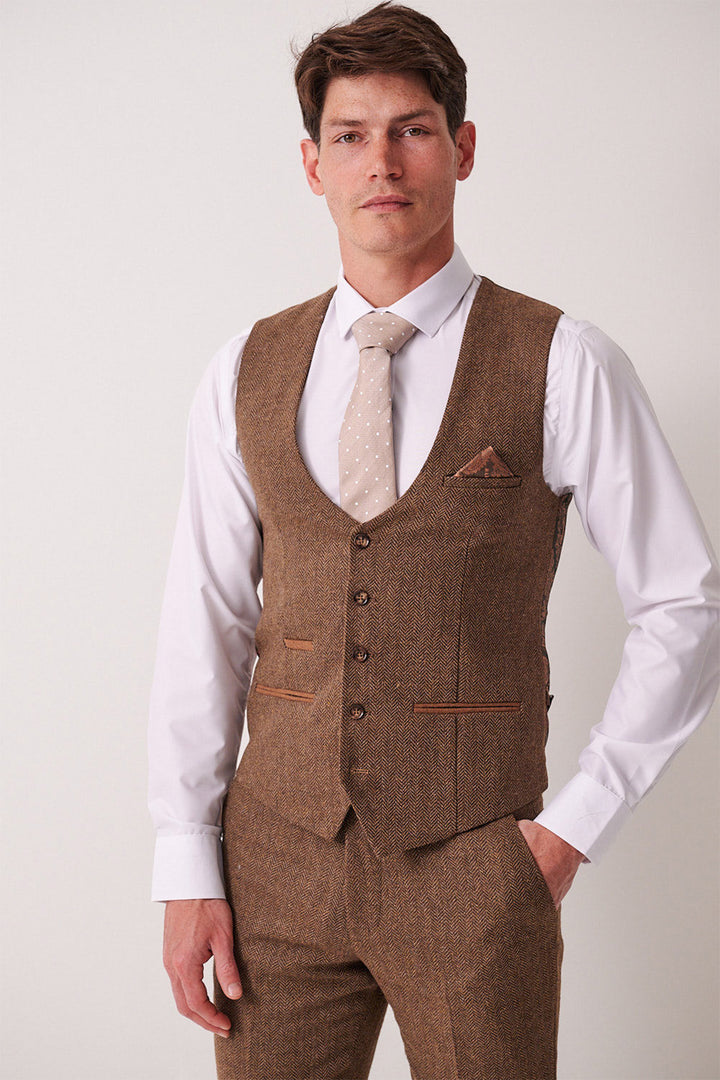 A man wears the marcdarcy DEAN Tan Tweed Three Piece Suit—featuring a slim fit vest and trousers, white dress shirt, and a light beige polka dot tie—standing against a plain light background.