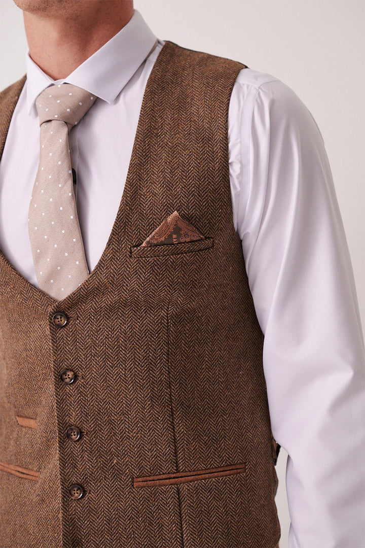 A man wears the marcdarcy DEAN Tan Tweed Three Piece Suit, featuring a brown herringbone vest, white shirt, light brown polka dot tie, and matching pocket square. The slim-fit look is cropped at shoulders and mid-chest.