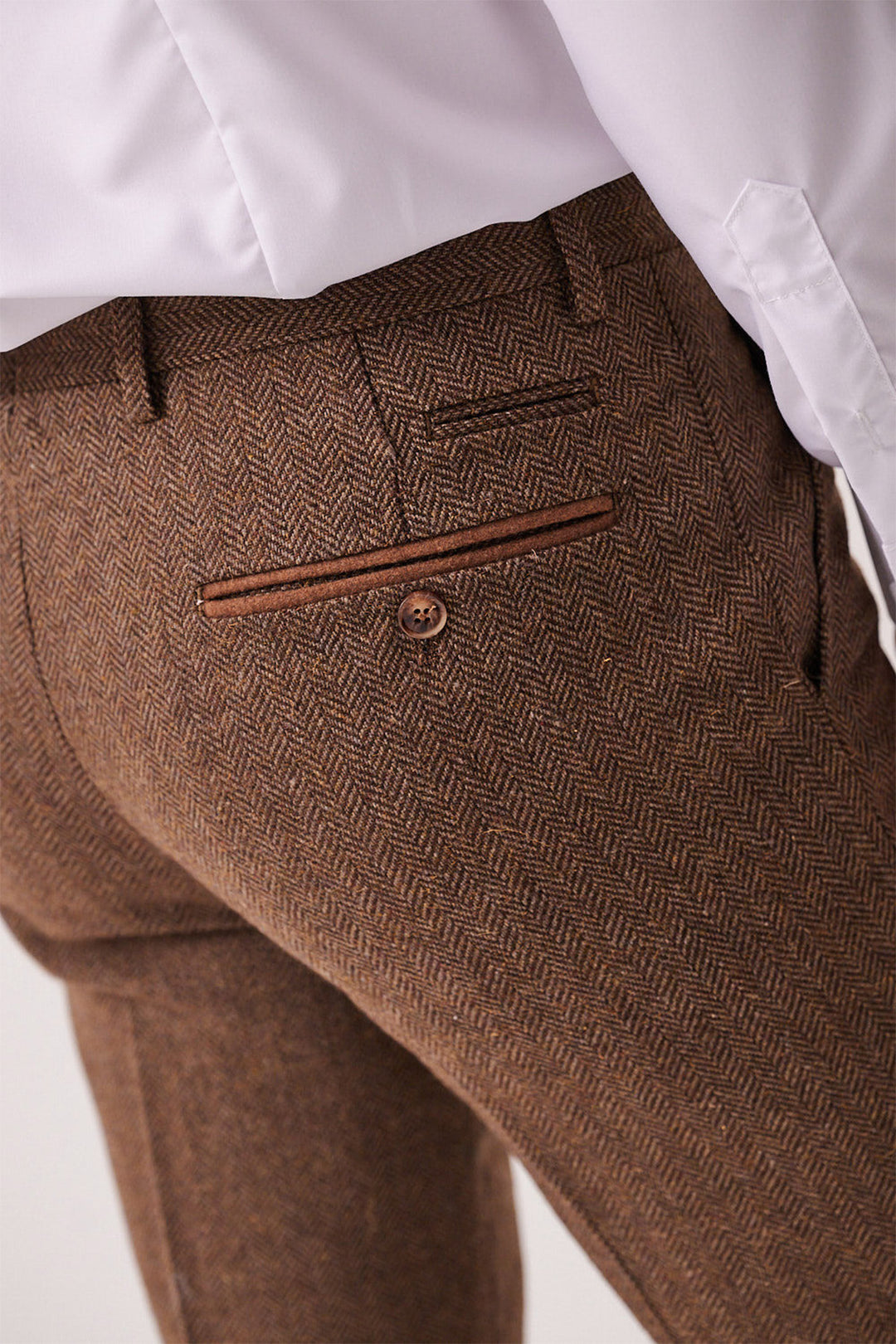 Close-up of a person wearing marcdarcy's DEAN - Tan Tweed Trousers in brown herringbone, featuring a slim fit, buttoned back pocket, and a white dress shirt tucked in.