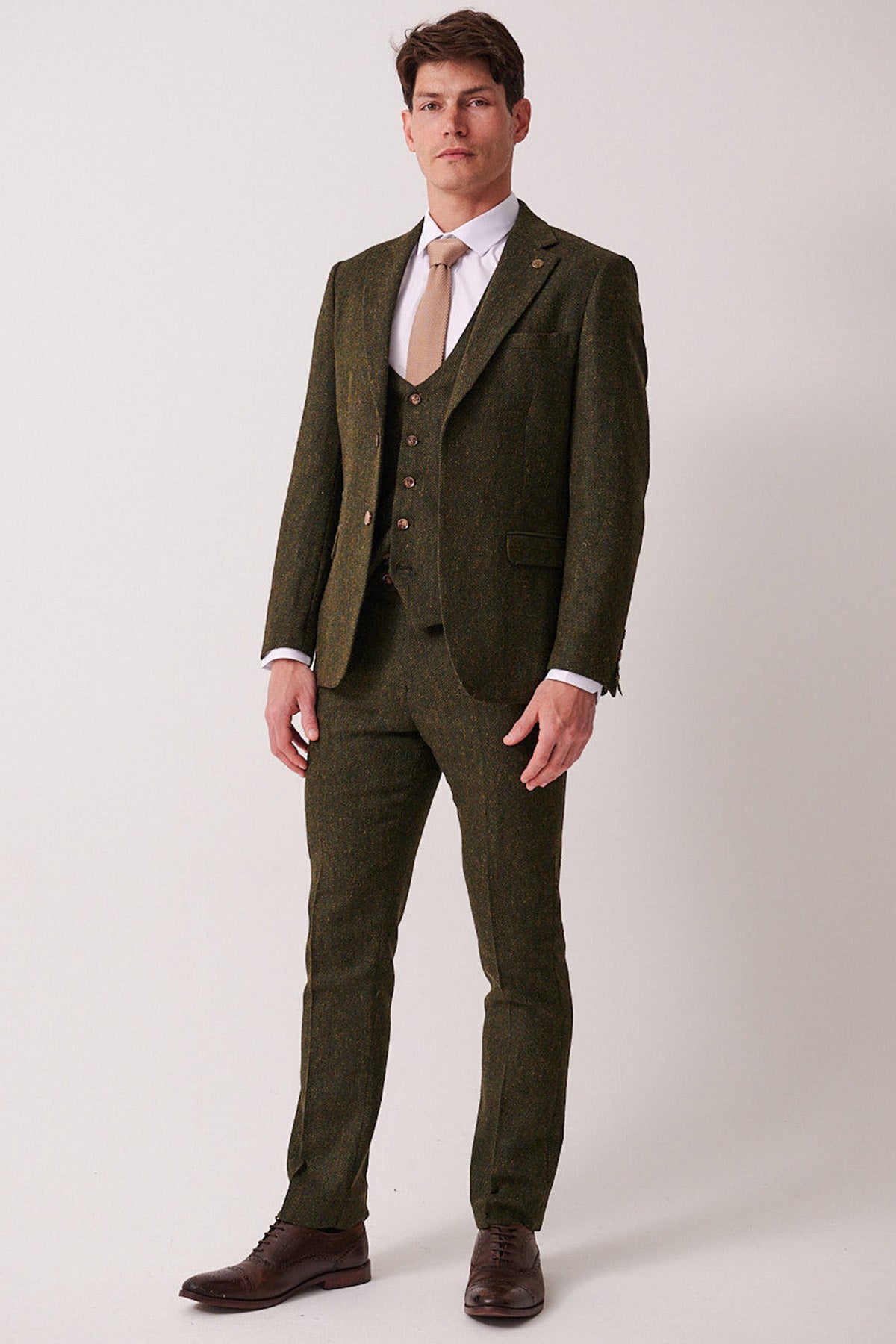 A man models the marcdarcy DEAN Olive Tweed Three Piece Suit, styled with a light tan tie and brown dress shoes, set against a white background.