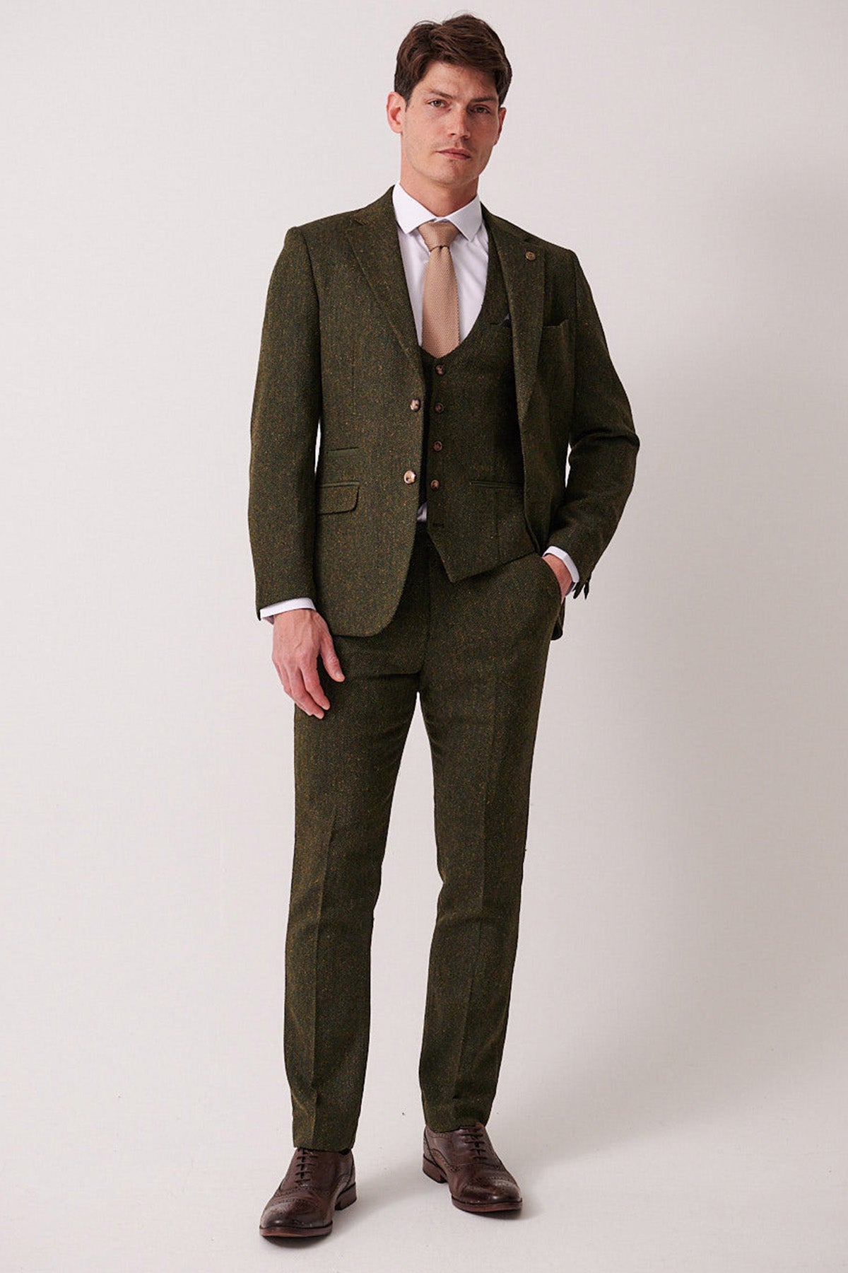 A man models the marcdarcy DEAN Olive Tweed Three Piece Suit, featuring a slim-fit blazer, paired with a white shirt and tan tie.