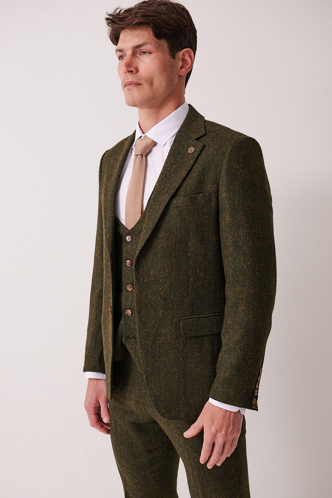 A man in the marcdarcy DEAN Olive Tweed Blazer with a beige tie stands against a white background, looking slightly to the side.