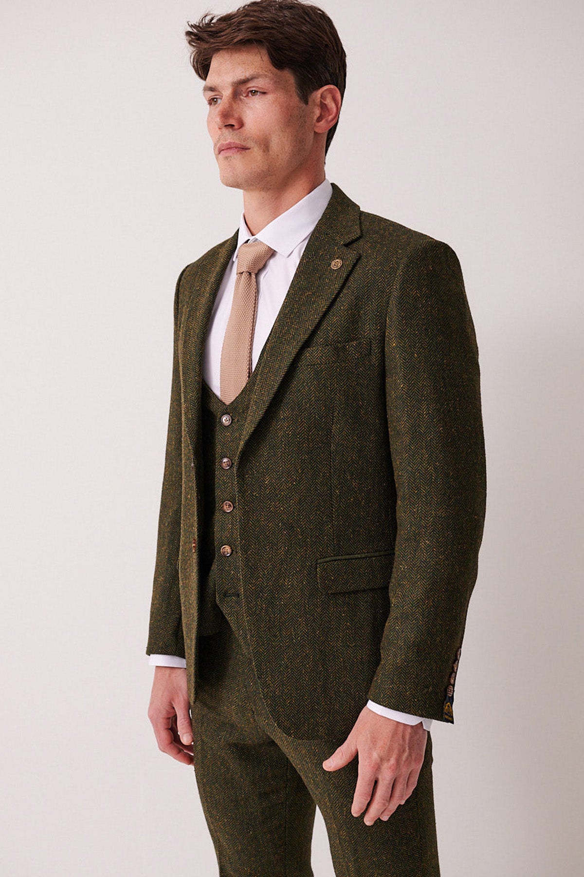 A man in the marcdarcy DEAN Olive Tweed Blazer with a beige tie stands against a white background, looking slightly to the side.