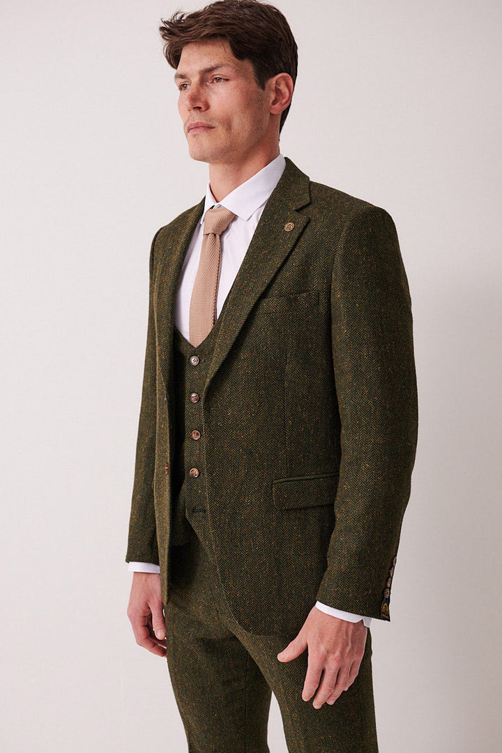 A man in the marcdarcy DEAN Olive Tweed Blazer with a beige tie stands against a white background, looking slightly to the side.
