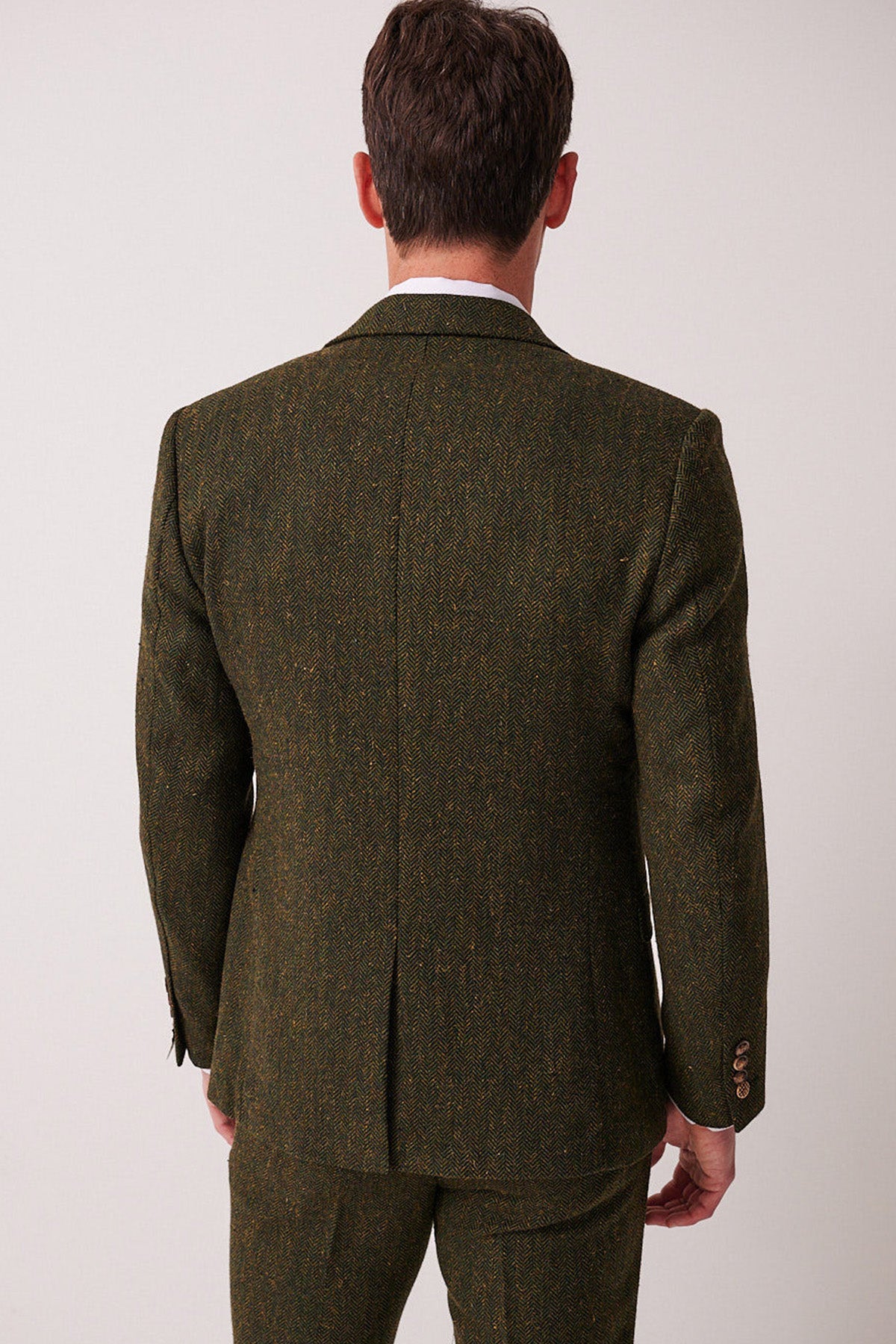 A man faces away from the camera, displaying the back of his marcdarcy DEAN Olive Tweed Blazer and trousers against a plain light background.