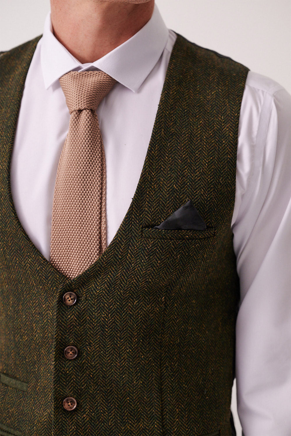 A man wears the Marc Darcy DEAN Olive Tweed Waistcoat over a white dress shirt, paired with a beige textured tie and black pocket square; only his upper torso is shown.