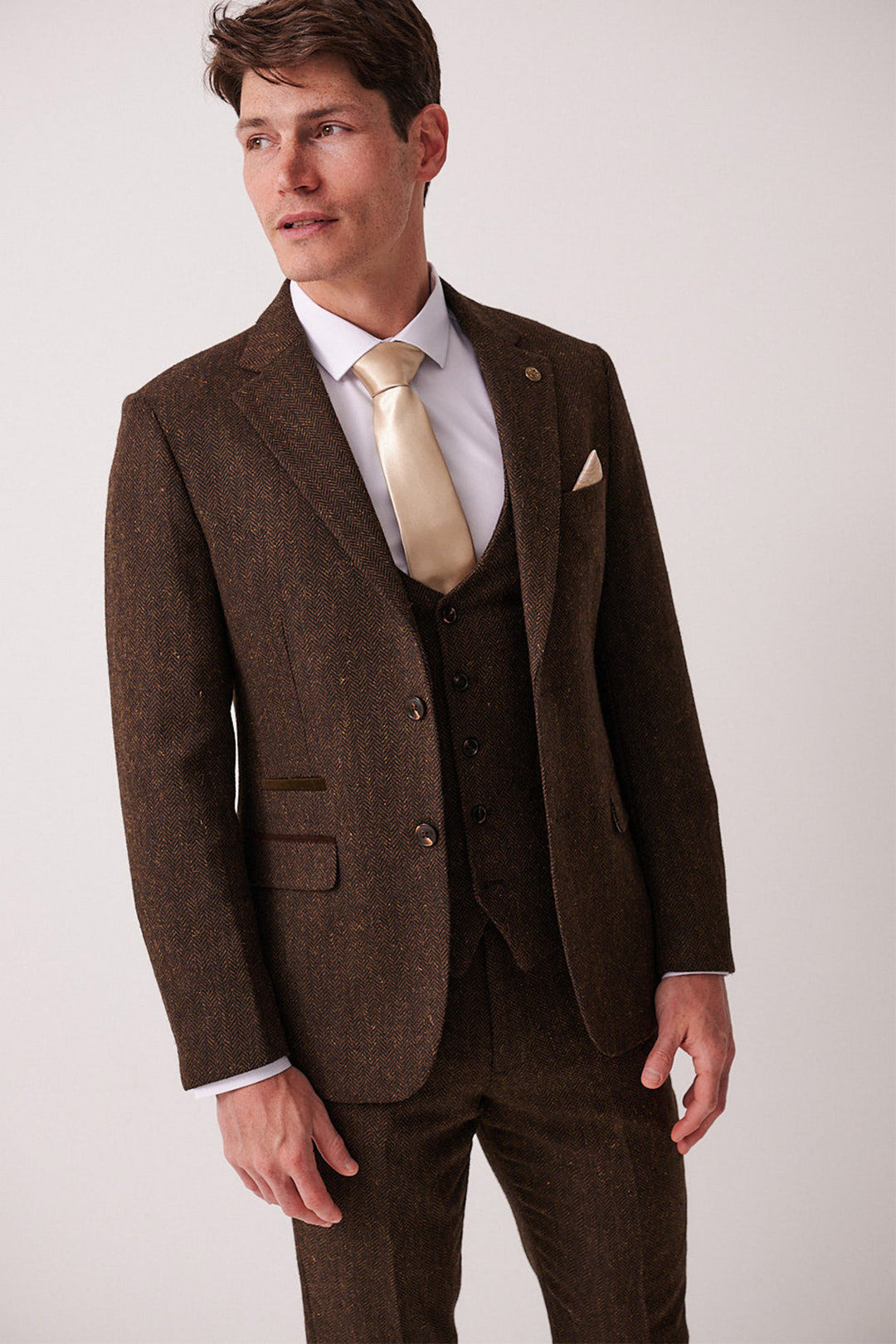 A man in the marcdarcy DEAN Brown Tweed Blazer, styled slim fit with a white dress shirt and gold tie, stands against a plain light background looking off to the side.
