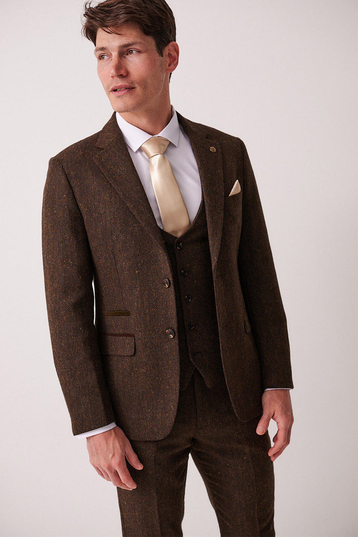 A man in the marcdarcy DEAN Brown Tweed Blazer, styled slim fit with a white dress shirt and gold tie, stands against a plain light background looking off to the side.
