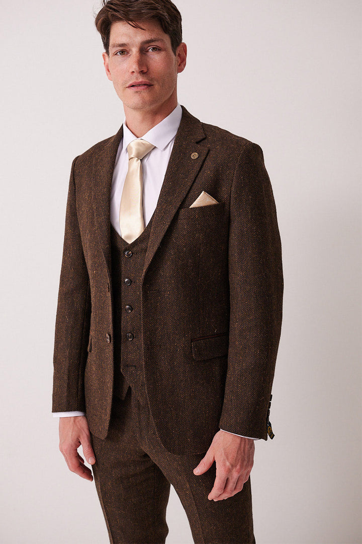 A man faces forward with a neutral expression, wearing the marcdarcy DEAN Brown Tweed Blazer over a white shirt, cream tie, and matching pocket square against a plain background.