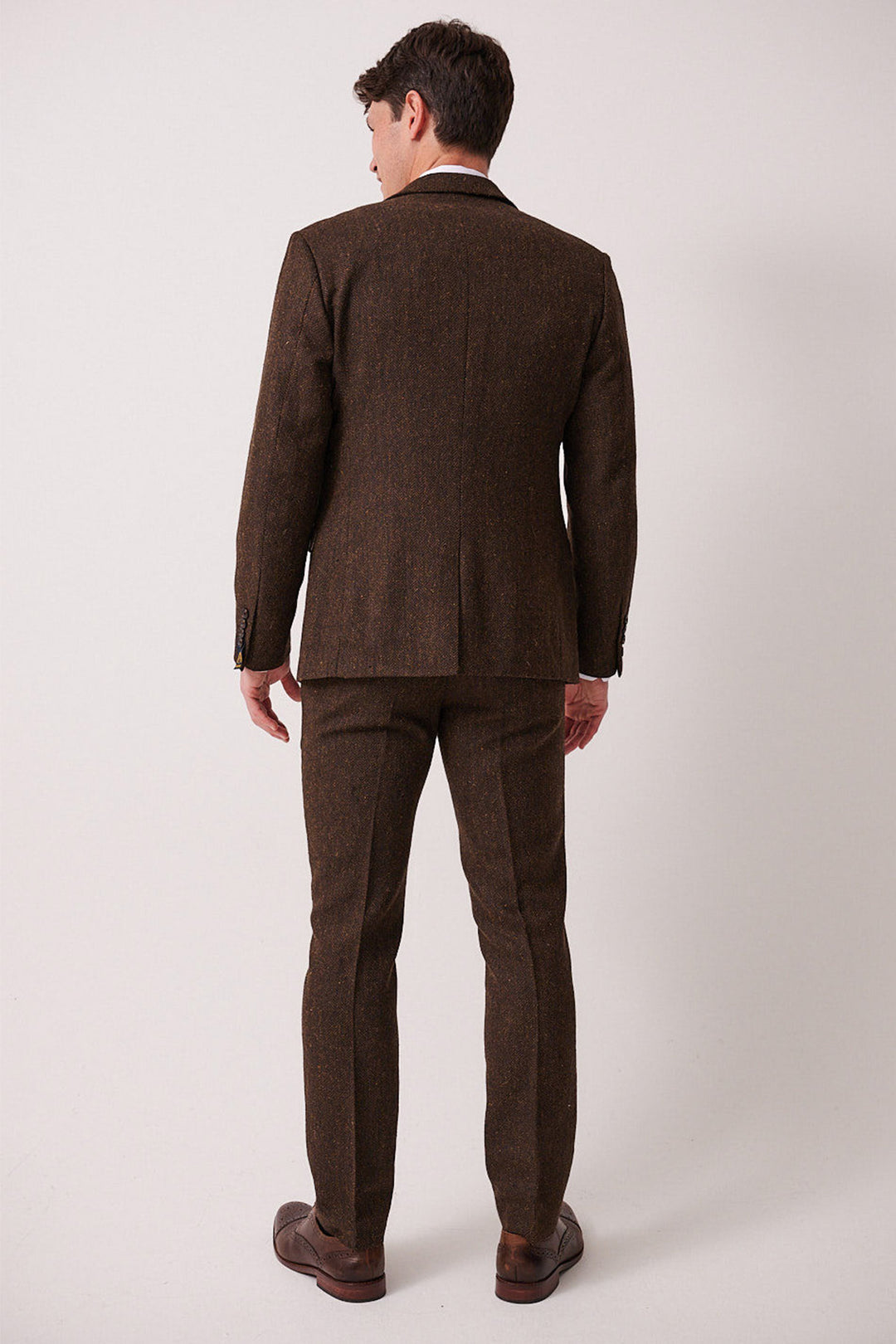 A man faces away from the camera wearing the marcdarcy DEAN Brown Tweed Three Piece Suit, paired with brown dress shoes, set against a plain white background.