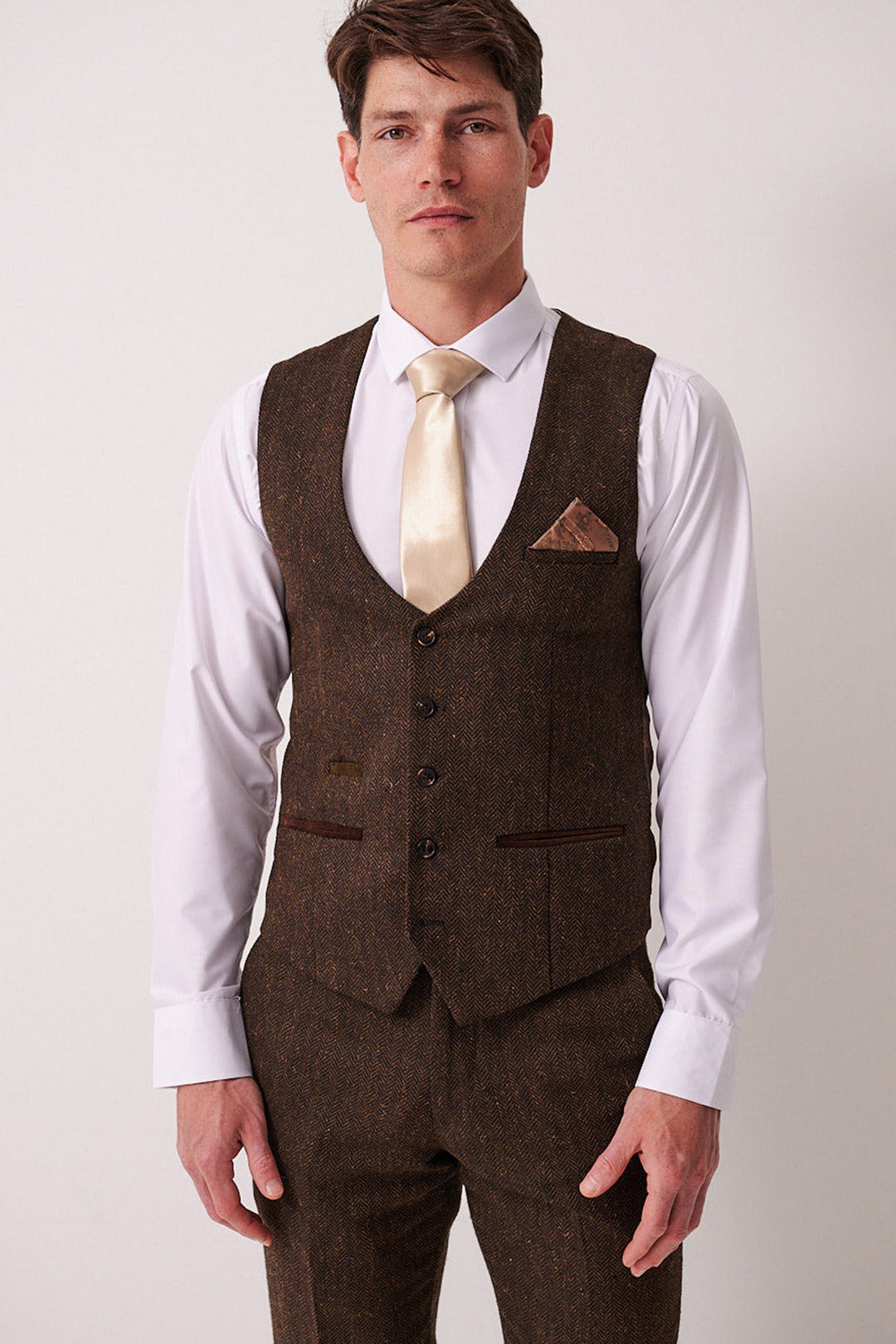 A man in a Marc Darcy DEAN brown tweed waistcoat and matching trousers, styled with a white shirt, cream tie, and brown pocket square, stands against a plain white background.