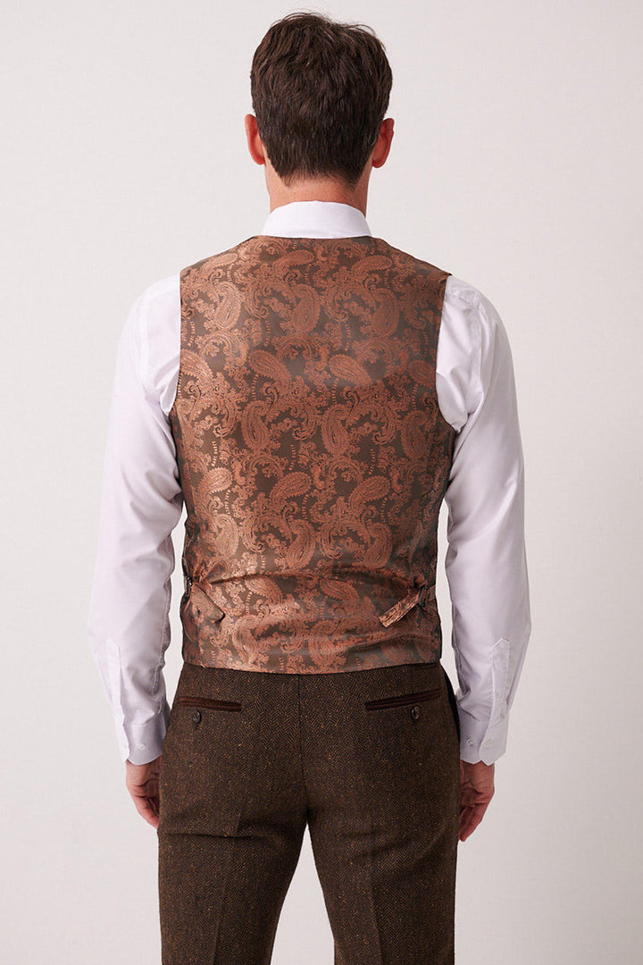 A man faces away from the camera wearing the marcdarcy DEAN Brown Tweed Three Piece Suit. The suit features a white dress shirt, brown waistcoat, and matching trousers against a plain, neutral background.