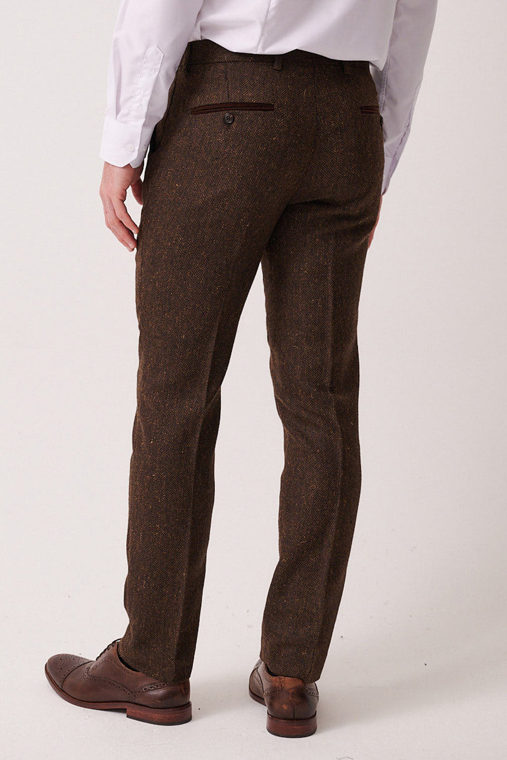 A person stands with their back to the camera against a plain light background, wearing marcdarcy's DEAN - Brown Tweed Trousers paired with a white dress shirt and brown dress shoes.