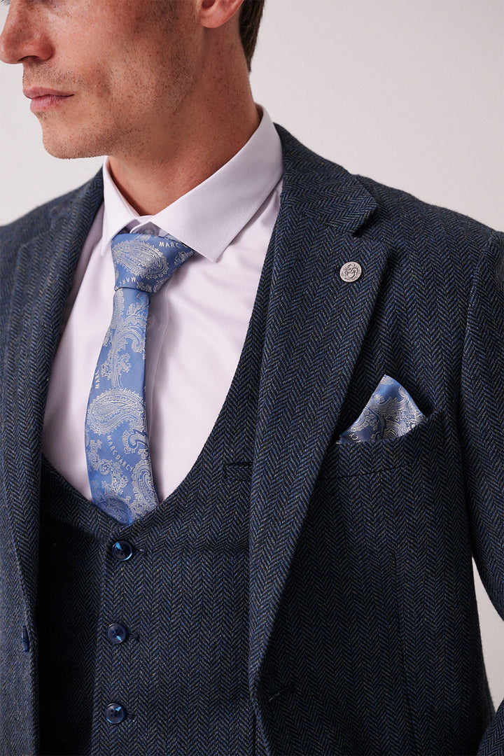 A man wears the marcdarcy DEAN Blue Tweed Three Piece Suit with a light purple shirt, blue patterned tie, and matching pocket square. Only his lower face and upper body are visible.