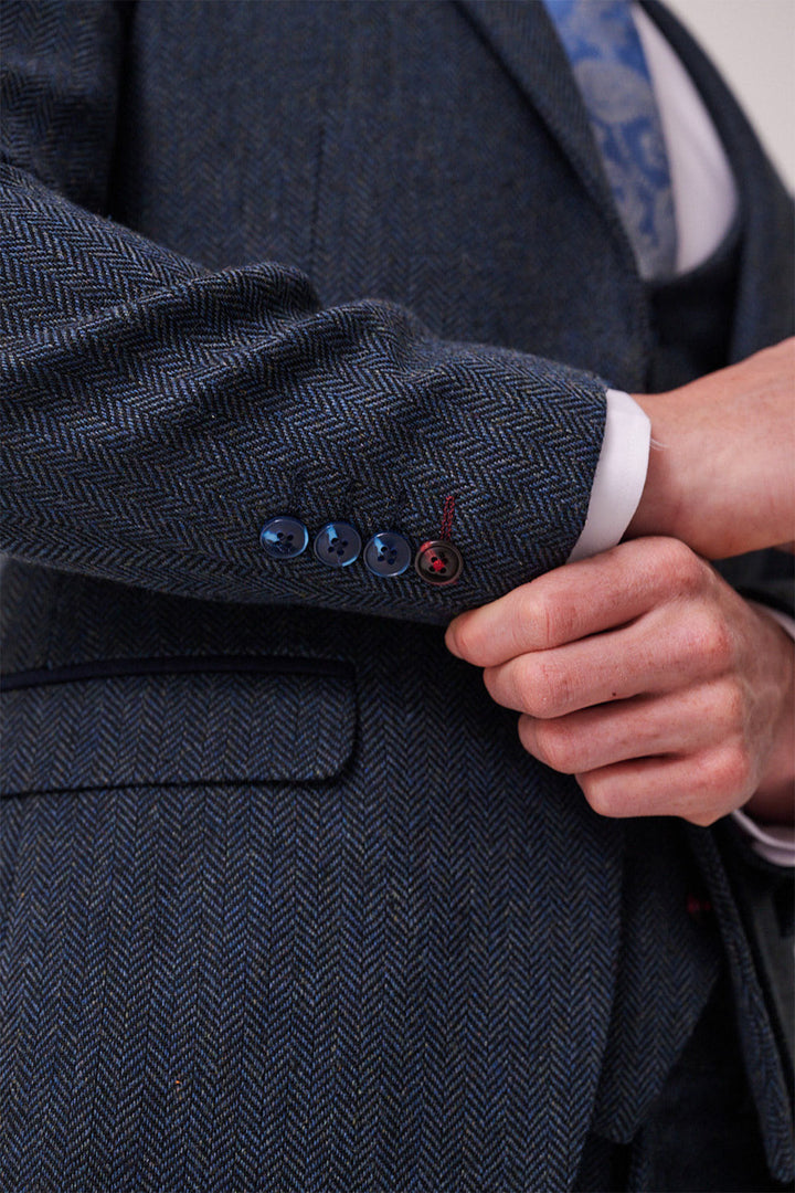 A close-up of a person adjusting the sleeve of the marcdarcy DEAN Blue Tweed Three Piece Suit, highlighting four cuff buttons and a hint of a blue patterned tie.