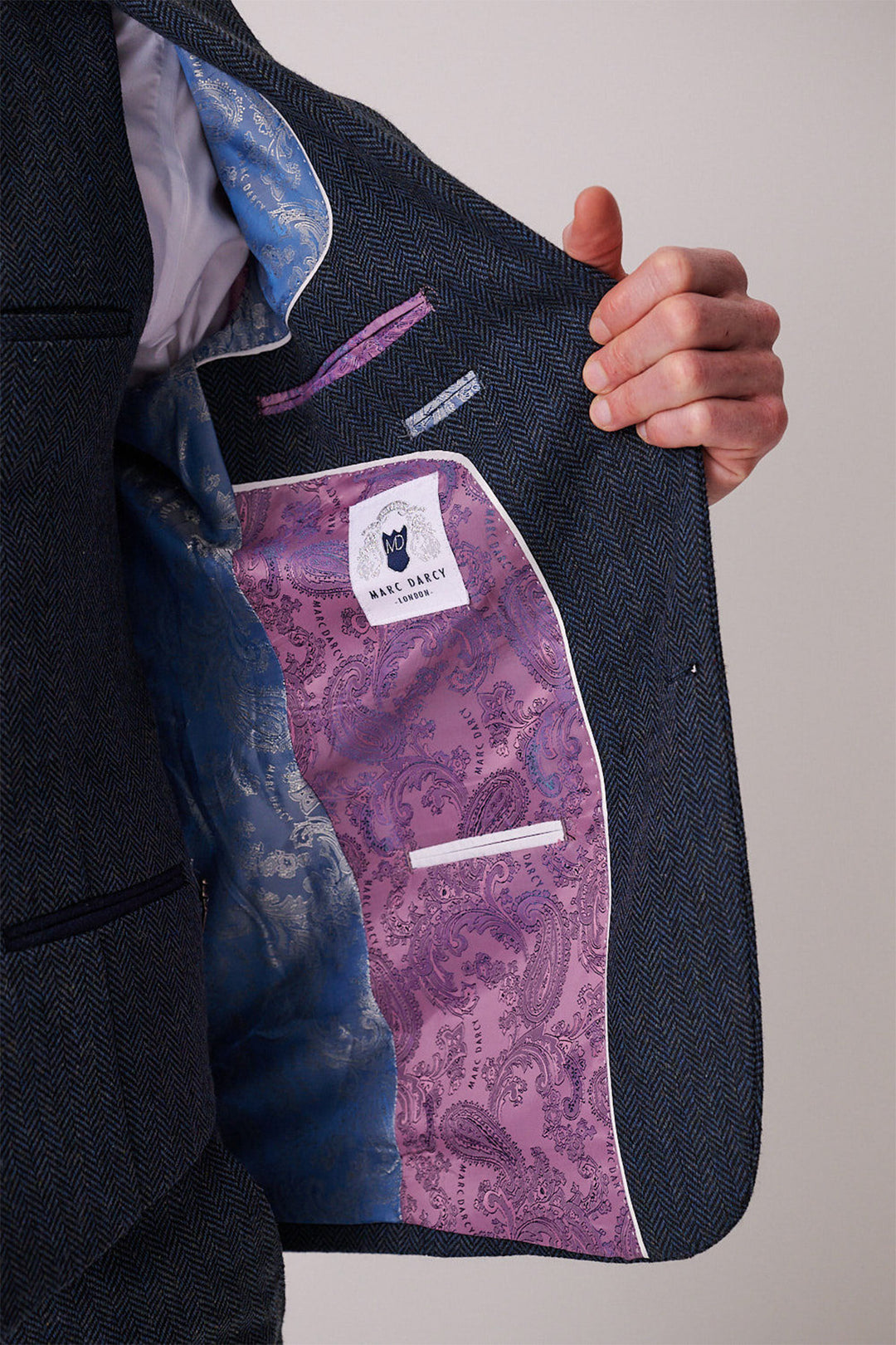 A person opens a marcdarcy DEAN Blue Tweed Three Piece Suit blazer to show its ornate blue and purple paisley lining and a white label reading “HIS SINCE.”.