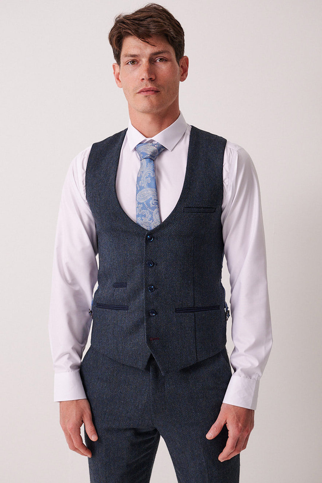 A man wears the Marc Darcy DEAN Blue Tweed Waistcoat over a white shirt and a light blue paisley tie, creating a refined slim fit look.