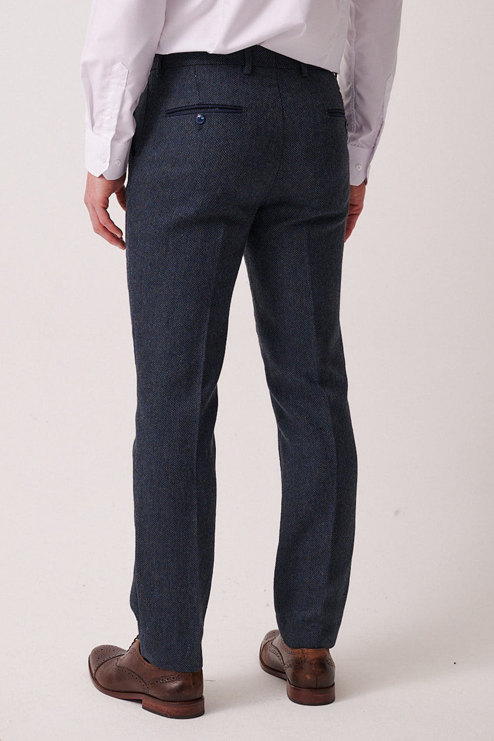 A man in marcdarcy’s DEAN Blue Tweed Trousers, a white dress shirt, and brown dress shoes stands with his back to the camera against a plain light background.