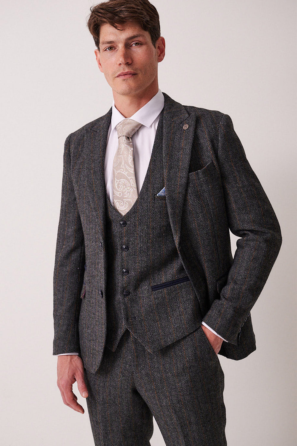 A man wears the marcdarcy DOMINIC Blue Grey Tweed Blazer with a white dress shirt and patterned tie, standing confidently against a plain light background.