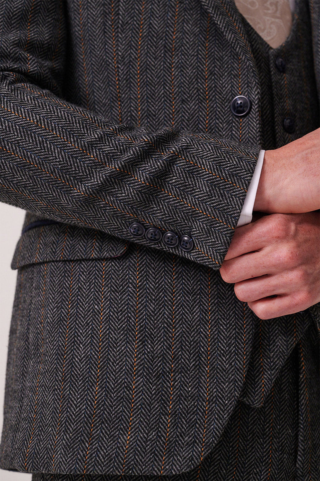 Close-up of a person adjusting the cuff of the marcdarcy DOMINIC Blue Grey Tweed Blazer, highlighting slim fit tailoring, button details, thin brown stripes in herringbone, and a glimpse of the matching vest underneath.