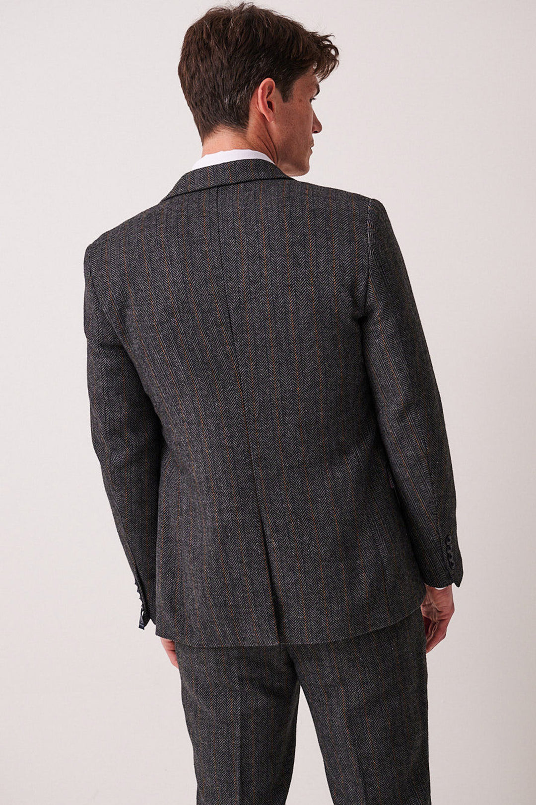 A man is seen from behind in the marcdarcy DOMINIC Blue Grey Tweed Three Piece Suit, standing against a plain light background and gazing slightly to his left.