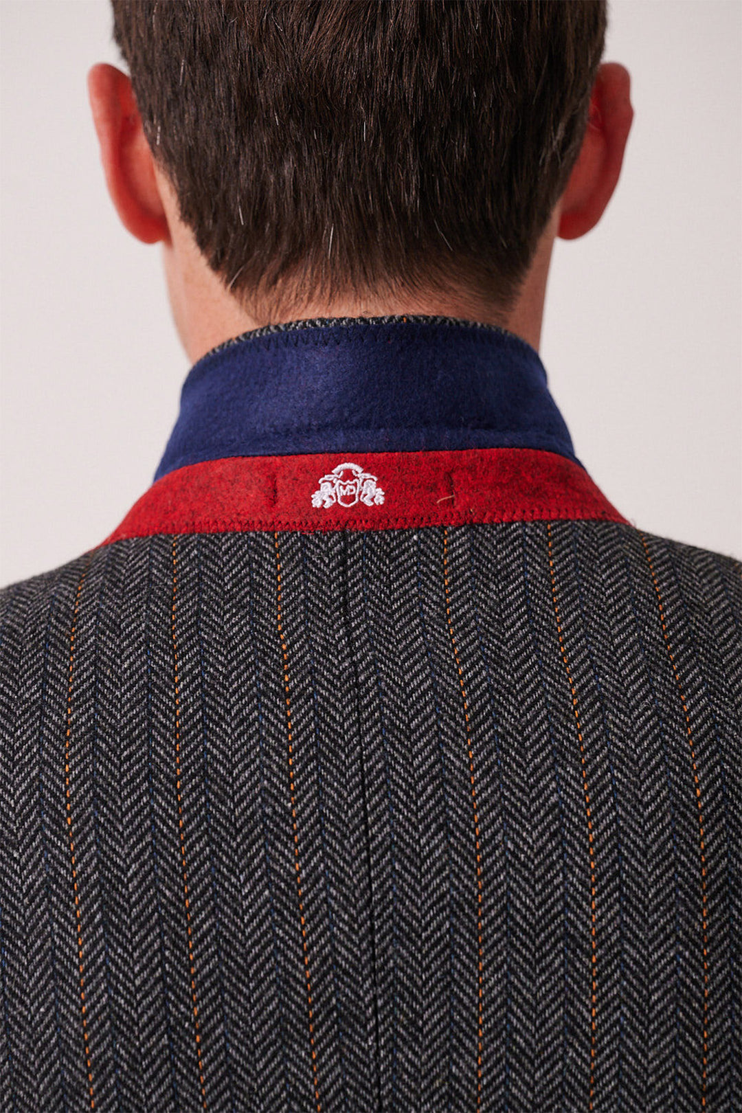 A close-up of a man's back features the marcdarcy DOMINIC Blue Grey Tweed Three Piece Suit, styled slim fit with herringbone pattern and orange pinstripes, plus a turned-up collar showing blue lining with red trim and white embroidery.