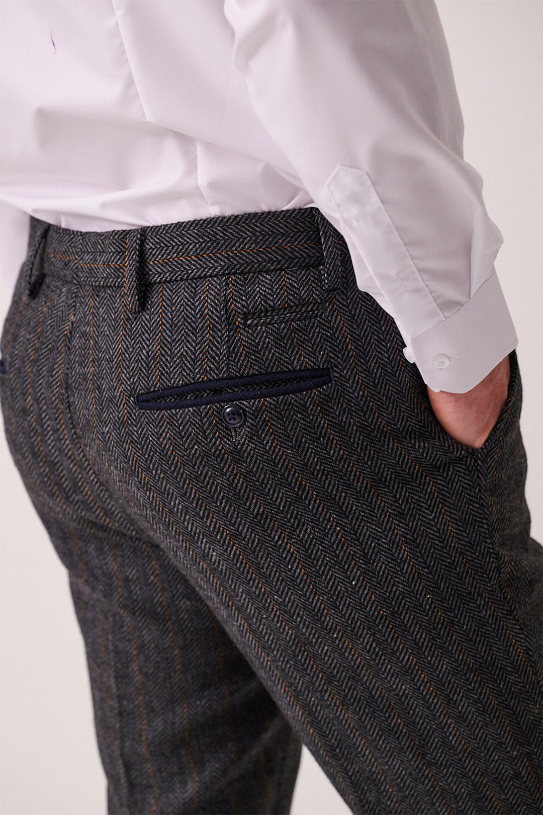 Someone is shown from the back at waist level, wearing marcdarcy DOMINIC blue grey tweed trousers in a slim fit herringbone pattern and a white dress shirt, with one hand in their pocket.