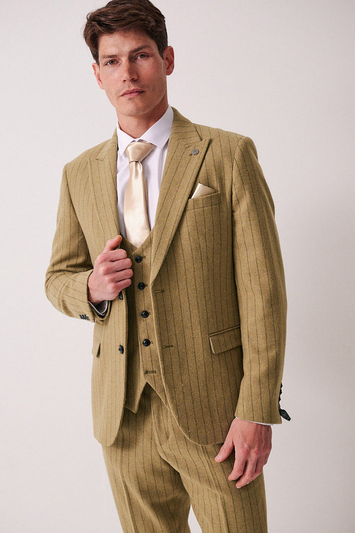 A man wearing the marcdarcy HANSON - Moss Tweed Pinstripe Blazer with a matching vest, white shirt, and cream tie stands facing forward, adjusting his jacket.