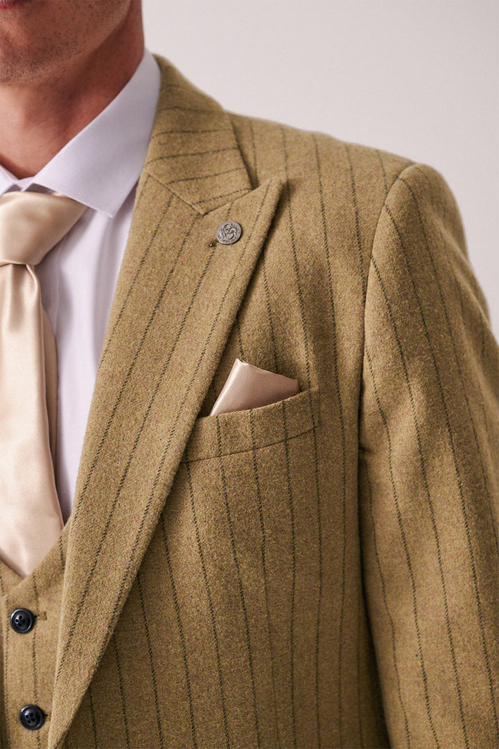 Close-up of a person wearing the marcdarcy HANSON Moss Tweed Pinstripe Blazer, paired with a beige tie, matching pocket square, white dress shirt, and silver lapel pin. The focus is on the chic upper chest and shoulder area.