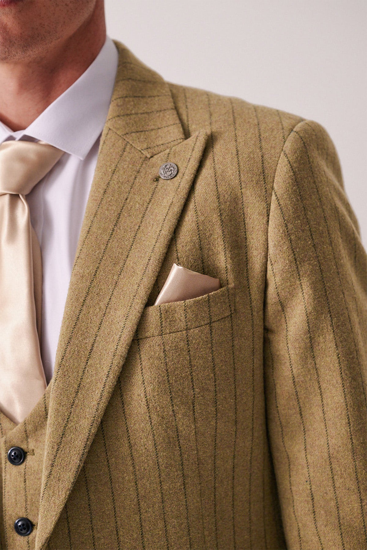 Close-up of a person wearing the marcdarcy HANSON Moss Tweed Pinstripe Three Piece Suit with matching vest, cream tie, white shirt, and a beige pocket square in the breast pocket.