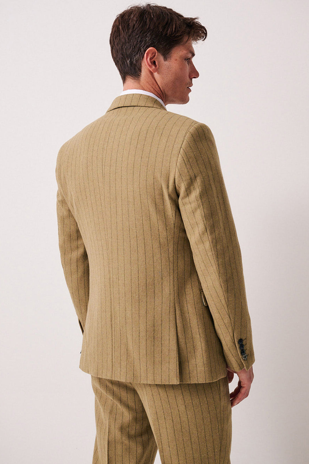 A man stands with his back to the camera, turning slightly to the side in a plain light setting, wearing the marcdarcy HANSON - Moss Tweed Pinstripe Blazer.