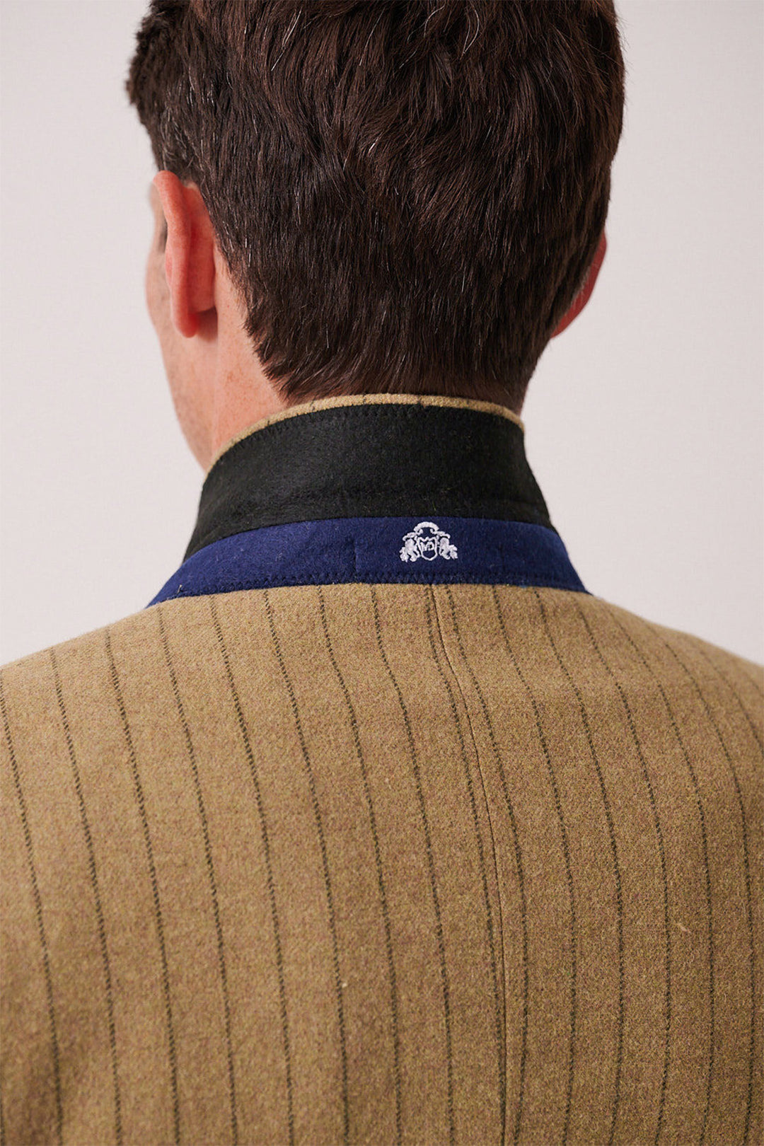 Back view of a person in the marcdarcy HANSON - Moss Tweed Pinstripe Three Piece Suit, featuring a brown pinstriped jacket with a black and blue collar, white embroidered detail on the back of the collar, and short brown hair visible.