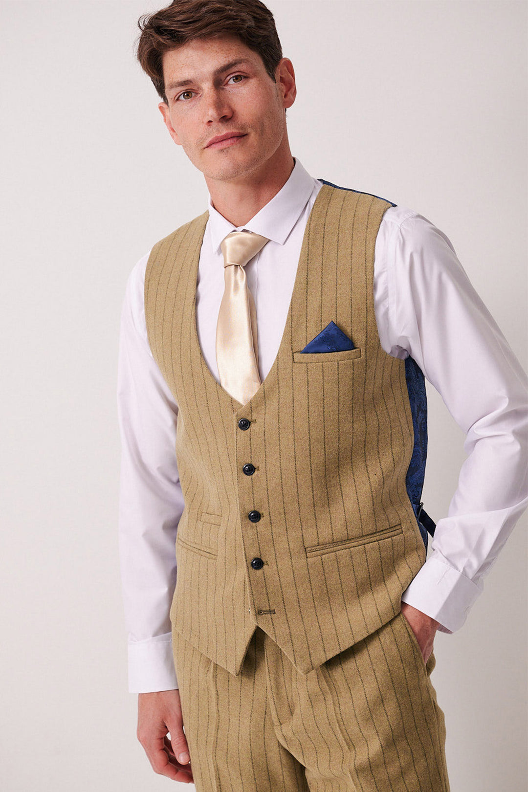 A man wears a Marc Darcy HANSON Moss Tweed Pinstripe Waistcoat with matching trousers, a white shirt, gold tie, and blue pocket square, standing against a light background and gazing neutrally toward the camera.
