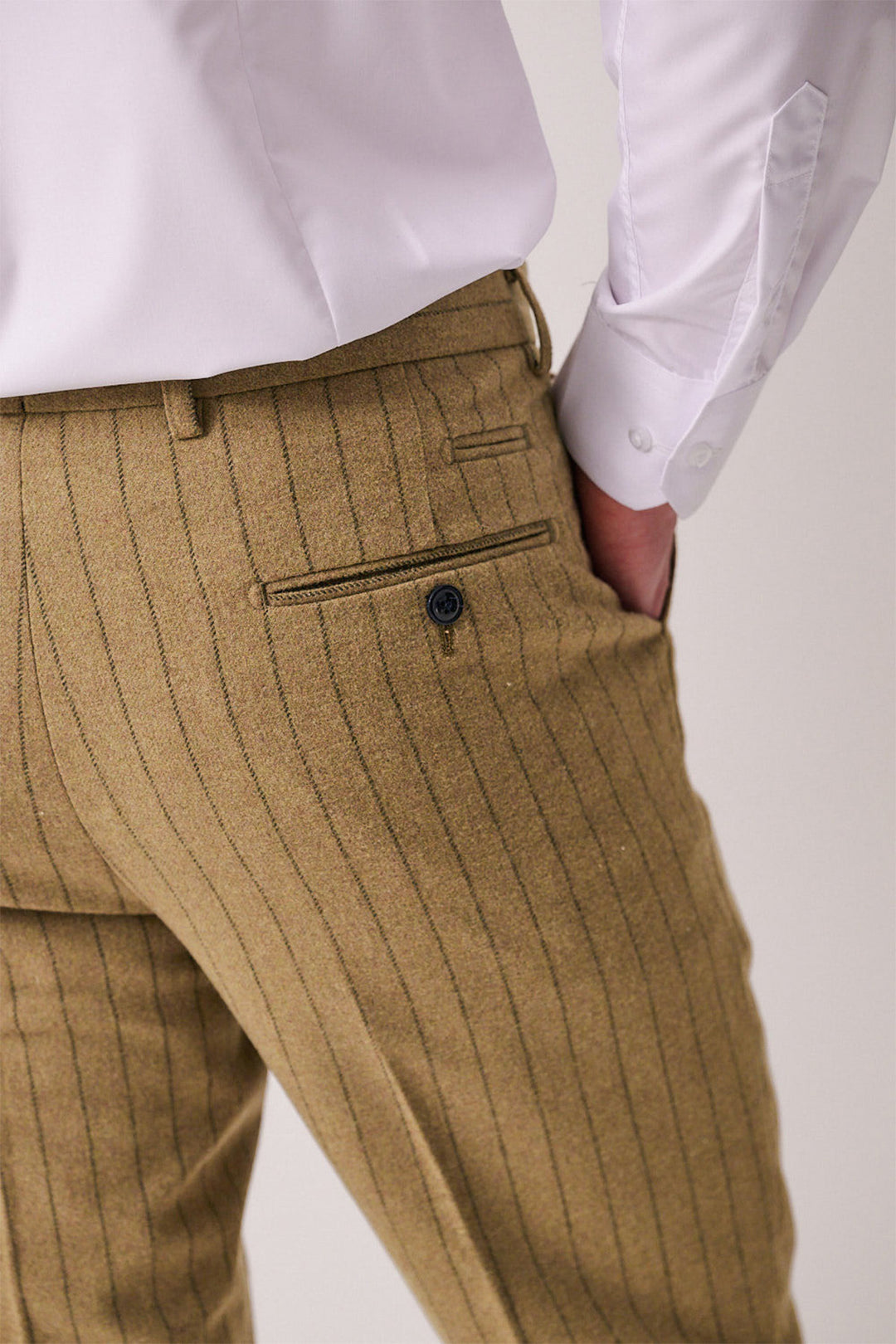 A person wearing marcdarcy HANSON - Moss Tweed Pinstripe Trousers in slim fit tan with a back pocket, paired with a white dress shirt; the shirt cuff and part of the hand are visible.