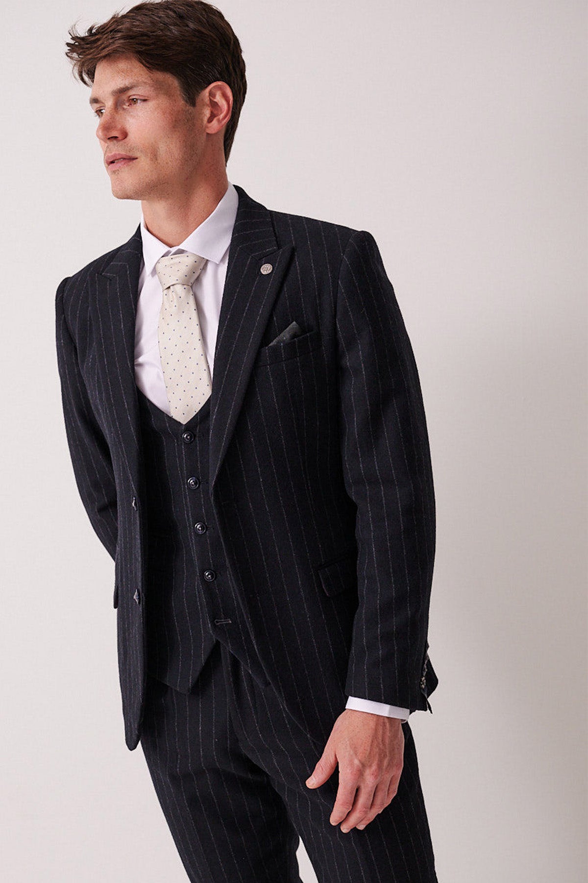 A man wears the marcdarcy HANSON Navy Tweed Pinstripe Blazer with a white dress shirt and light-colored tie, standing against a plain light background and smiling slightly while looking to the side.
