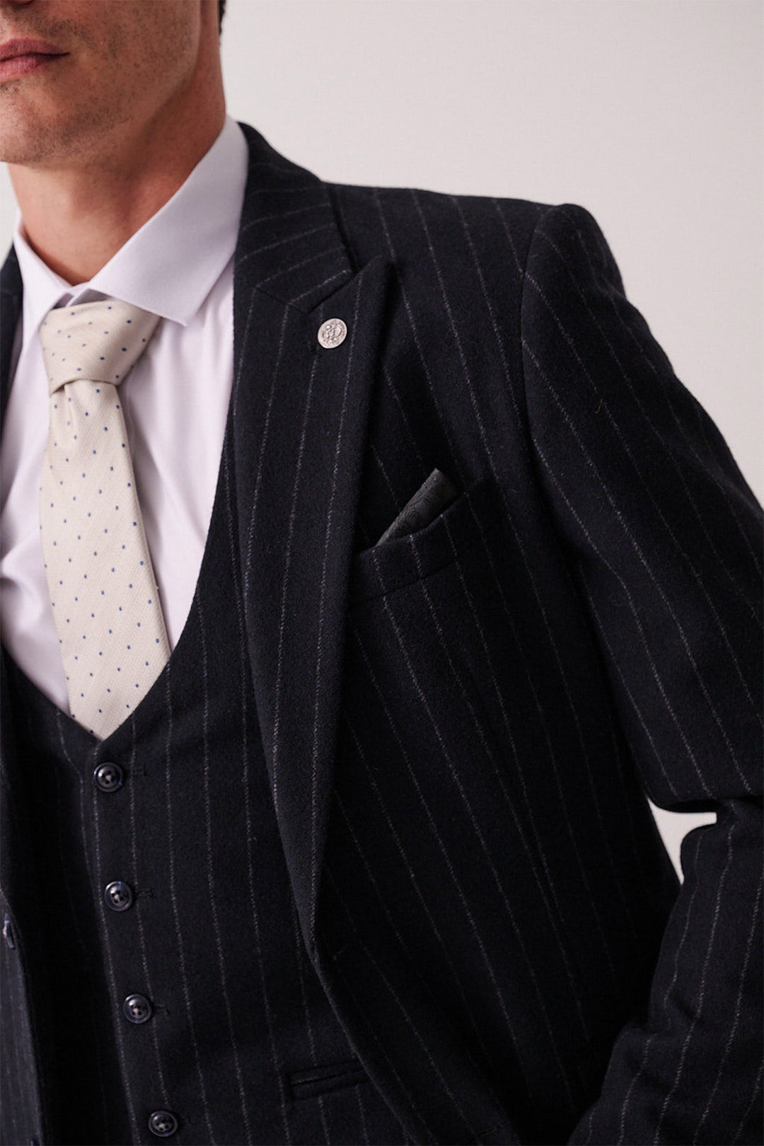 A close-up of a person wearing the marcdarcy HANSON Navy Tweed Pinstripe Three Piece Suit with a white shirt, light-patterned tie, pocket square, and lapel pin; their face is partially out of frame.