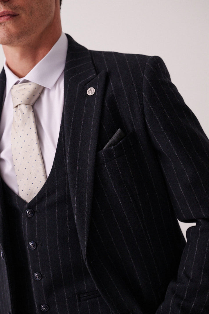 A close-up of a person wearing the marcdarcy HANSON Navy Tweed Pinstripe Three Piece Suit with a white shirt, light-patterned tie, pocket square, and lapel pin; their face is partially out of frame.