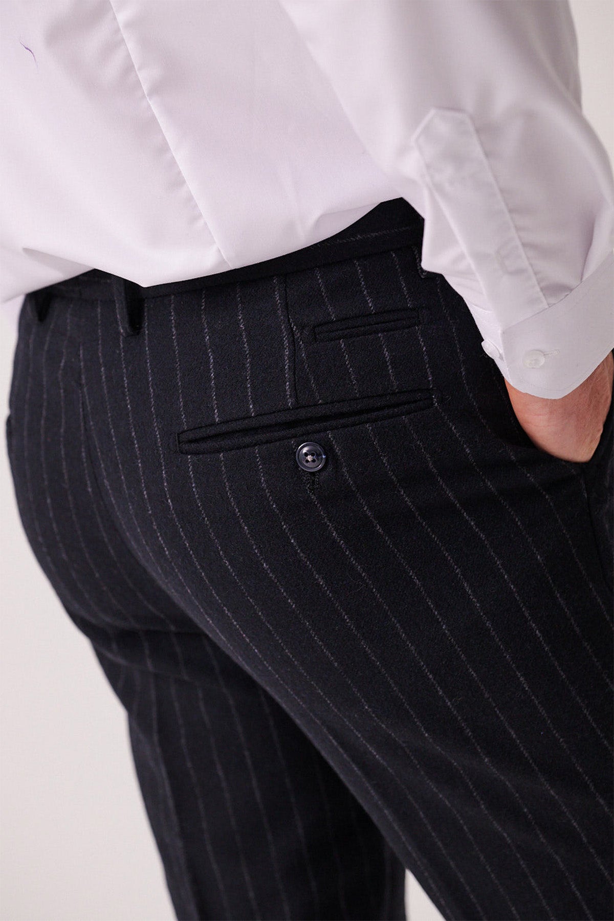 A person wears a white dress shirt and marcdarcy’s HANSON Navy Tweed Pinstripe Trousers, hand in the back pocket. The image spotlights the waist and upper legs, highlighting the textured fabric and button detail.