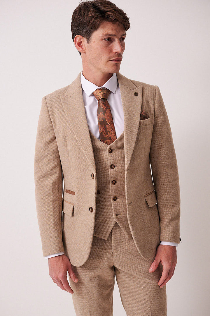 A man with short brown hair models the marcdarcy HAYDEN - Oak Crossweave Three Piece Suit, styled slim fit with a white shirt and patterned brown tie, standing slightly sideways against a plain light background.