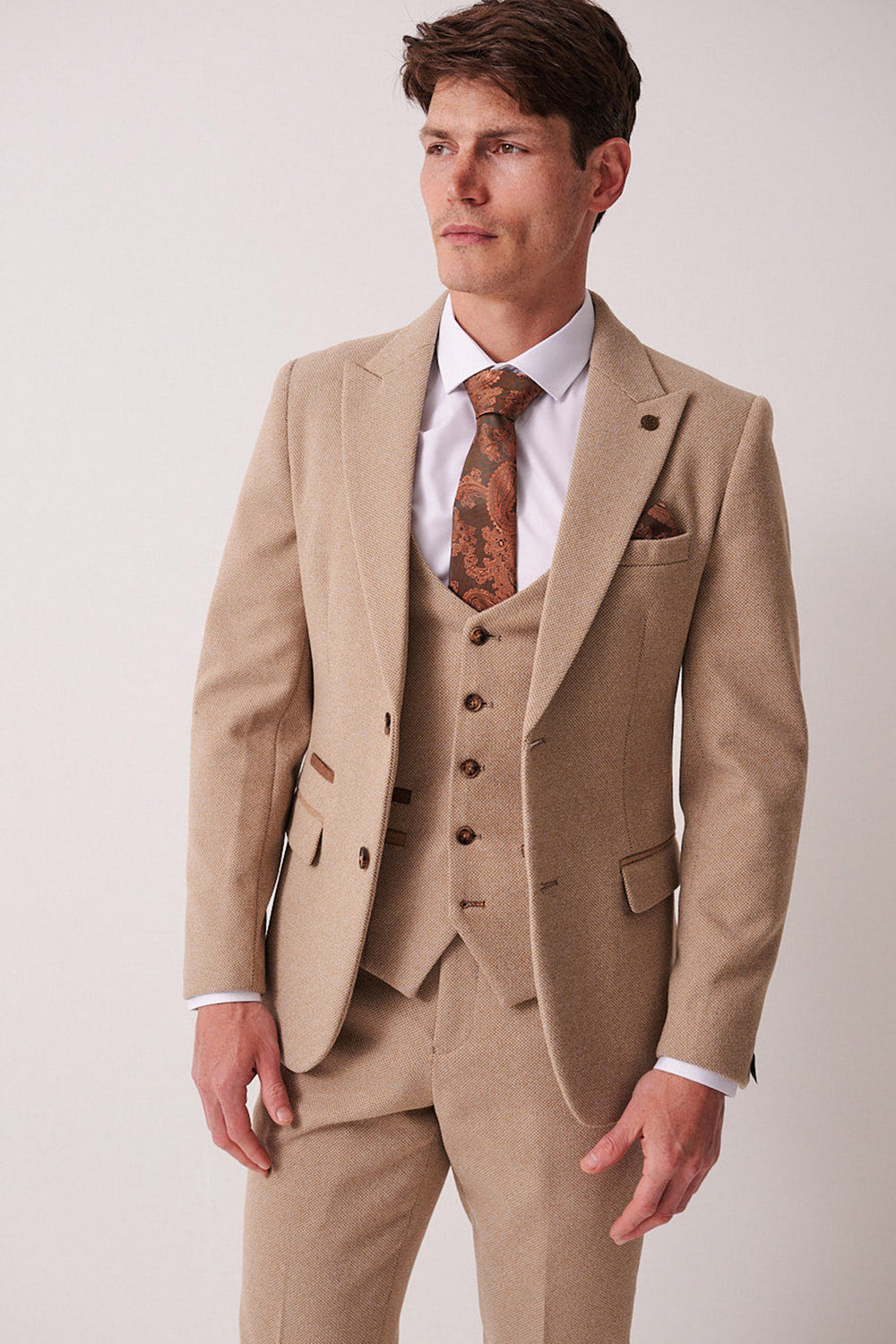 A man in the marcdarcy HAYDEN - Oak Crossweave Blazer, paired with a beige three-piece suit, white shirt, and patterned brown tie, stands against a plain light background, looking slightly to his left.