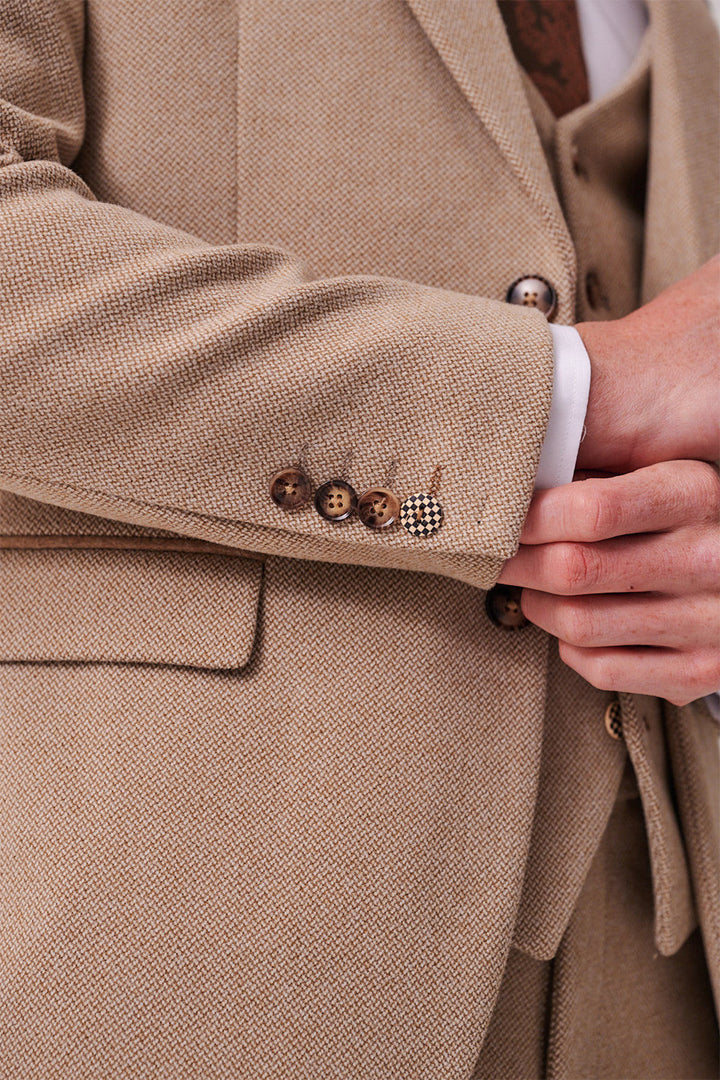 Close-up of a person adjusting the cuff of a marcdarcy HAYDEN - Oak Crossweave Three Piece Suit, featuring brown buttons, a white shirt cuff, and matching vest.