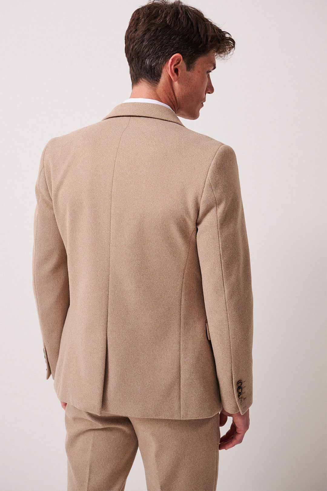 A man wearing the marcdarcy HAYDEN Oak Crossweave Blazer stands with his back to the camera, head turned slightly left, in matching trousers against a plain, light-colored background.