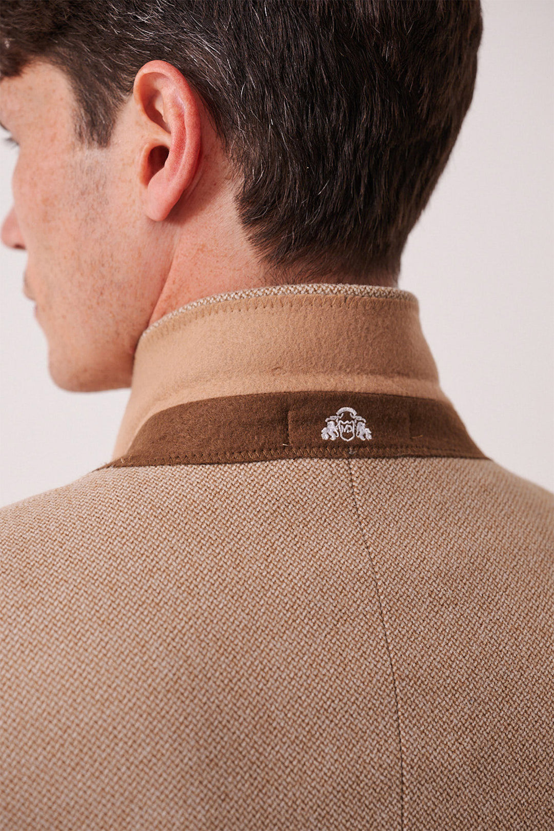 A close-up of a man's back and neck shows the marcdarcy HAYDEN - Oak Crossweave Three Piece Suit in tan and brown with a textured finish, standing collar, and a small white embroidered logo on the upper back.